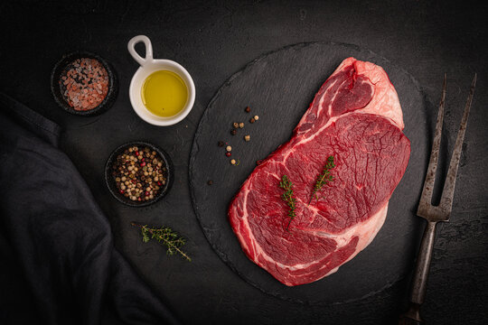 Raw fresh beef steak with spices on a dark slate, stone or concrete background. Top view with copy space. High quality photo