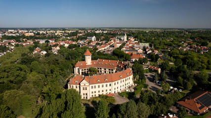 Fototapeta premium Aerial view of a charming Polish town with red-roof houses, a central square, and a historic castle surrounded by green trees. Beautiful European architecture on a sunny summer day.