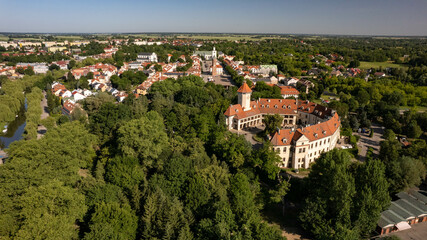 Obraz premium Aerial view of a charming Polish town with red-roof houses, a central square, and a historic castle surrounded by green trees. Beautiful European architecture on a sunny summer day.