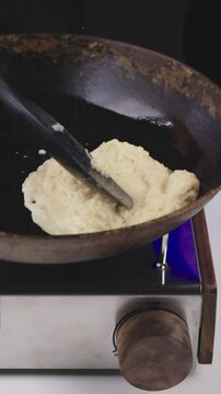 Raw potato mixture for draniki is placed onto a hot frying pan for cooking.