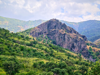 A panoramic view of green mountain ranges and foothills in Bostanliq District of Tashkent Region, Uzbekistan, stretching into the distance under a cloudy sky.