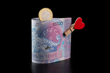 Banknotes of 10,000 Kazakhstani tenge and a clothespin with an image of a human heart on a black...
