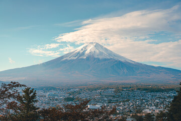 Fototapeta premium Cityscape views of the city near the volcano in the autumn from the Chureito Pagoda, Japan. There is Mount Fuji with snow on the top with a clear blue sky. There are colorful houses and buildings.