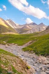 Fototapeta premium Wide-angle view of the mountains, rivers, and green grassy hills on both sides at Tianshan mountain, Xinjiang, Chaina. There are many rocks along the way. Idea for nature wallpaper.