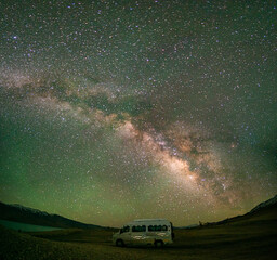 A stunning night sky showcases the Milky Way galaxy arching above a camper van parked at The high altitude Tso Moriri Lake in Ladakh, India,capturing the serenity and wonder of stargazing in nature