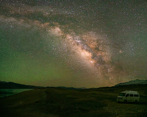 A stunning night sky showcases the Milky Way galaxy arching above a camper van parked at The high...