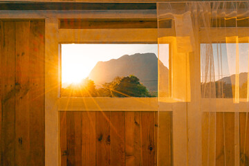 Wide-angle view of an open-air wooden bathroom. White-curtain windows offer views of the mountains and rays of sunlight in a warm tone. Idea for home design wallpaper with copy space.