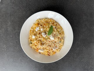 A creamy pumpkin risotto with goat cheese and fresh sage, beautifully served on a white plate and photographed from a top down view