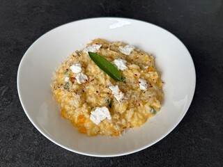 A creamy pumpkin risotto with goat cheese and fresh sage, beautifully served on a white plate and photographed from an angled view.