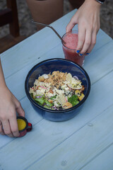 Blue bowl on a blue wooden table with red juice and a small sauce bowl, with hands interacting in the scene. A vibrant, fresh, and casual dining setup with natural light.
