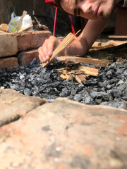 Hands arranging kindling and charcoal for an outdoor fire.