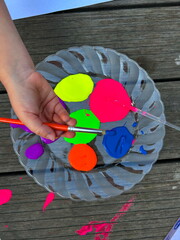 Bright neon gouache paints on a plate, a brush in the hands of a child. Children's creativity