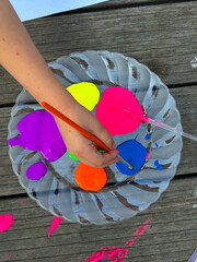 Bright neon gouache paints on a plate, a brush in the hands of a child. Children's creativity