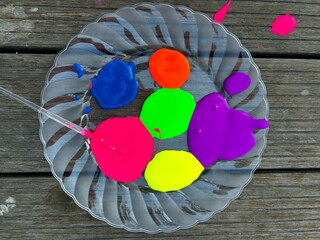Bright neon gouache paints on a plate, a brush in the hands of a child. Children's creativity