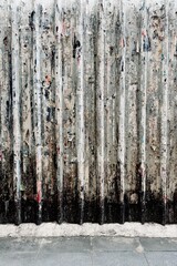 The corrugated metal surface is black and white, and the metal looks like it’s covered in layers of old posters, stickers, and advertisements that have been torn apart over time, leaving 