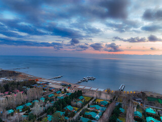Aerial view of Issyk Kul Lake under an overcast sunset sky, showing a coastal resort with buildings...