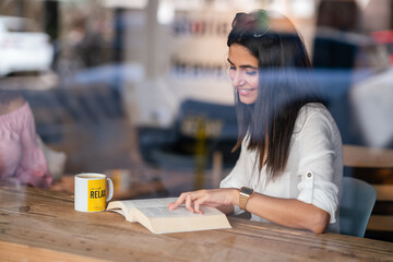 Young pretty woman is sitting and drink a glass lemonade while she is reading a book 