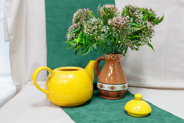 A yellow teapot sits on a green cloth next to a vase of flowers