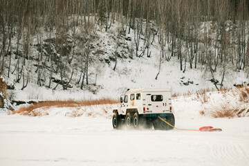 A white truck with a red hose attached to it is driving through a snowy field