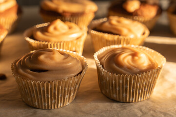Close-up of muffins with shiny icing in the warm light. The cream casts soft shadows on the pastries.