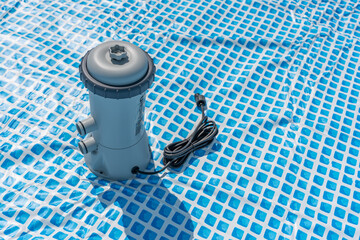 The pool pump is standing on the blue surface, the cable is wound up. It is ready for connection.