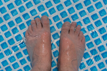 Both feet stand flat in the shallow pool water. Sunlight reflects on the skin and water surface.