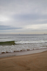 White foamy waves in a beautiful blue sea. In the distance, silhouettes of ships can be seen sailing near the coast of Gdansk on the Baltic Sea. Wave after wave rolled onto the shore. Background.