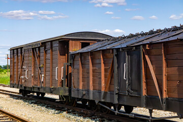 Obraz premium Historic wooden freight cars at the narrow-gauge railway station in Zbiersk, Greater Poland. The wagons feature dark wooden sides and black metal elements, captured on a sunny day at a heritage rail s
