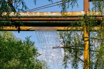Damaged industrial pipeline with a strong water leak. Rusty pipes run above dense vegetation on a...
