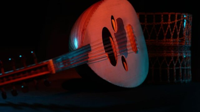 A static, cinematic shot of a traditional Middle Eastern Oud. Dramatic red and blue stage lighting highlights the ethnic string instrument against a dark, moody black background.