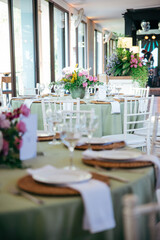 Wedding table with white chairs, white plates, and a floral arrangement featuring roses. A romantic and elegant setup for a wedding reception, blending simplicity, beauty, and natural charm.