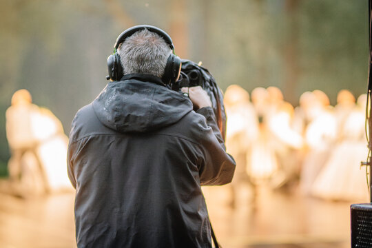 A cameraman films the  stage performance during a traditional outdoor concert, capturing scenes with a professional video camera.