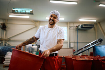 Happy worker carrying containers with sunflower seeds in a factory.