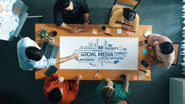 A diverse team engages in a collaborative meeting around a modern workspace table, analyzing social media strategies and trends through focused discussion and visual aids. Amity