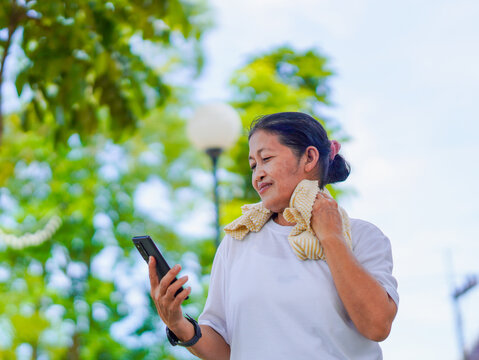 Happy senior woman enjoying using smartphone for online shopping, research browser, chat communication or checking fitness tracker after exercise in park holiday. Elderly use technology in lifestyle 