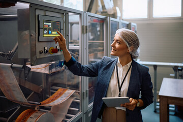 Company manager using touchpad while monitoring the processing machine in factory plant..