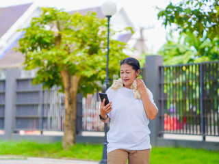 Happy senior woman enjoying using smartphone for online shopping, research browser, chat communication or checking fitness tracker after exercise in park holiday. Elderly use technology in lifestyle 