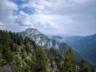 Mountain View Of Branderschrofen Peak In Bavaria: Jagged Summit Towering Over Forested Ridges Under Dramatic Skies In The Tegelberg Mountain Range, Germany
