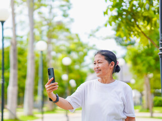 Happy senior woman enjoying using smartphone for video call, research browser, chat communication or calling to family after exercise in park holiday. Elderly use technology in lifestyle. Healthcare 