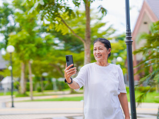Happy senior woman enjoying using smartphone for video call, research browser, chat communication or calling to family after exercise in park holiday. Elderly use technology in lifestyle. Healthcare 