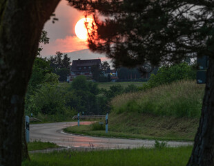 Sunset over winding road framed by trees and lush green fields in a tranquil rural landscape