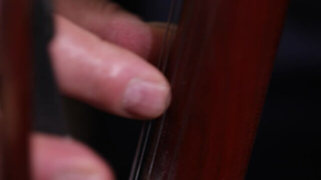An elegant close-up of a cellist's hand bowing strings. The shot shifts to the bridge, showing detailed, skilled technique during a classical music performance with beautiful bokeh.