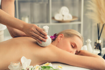 Hot herbal ball spa massage body treatment, masseur gently compresses herb bag on woman body....