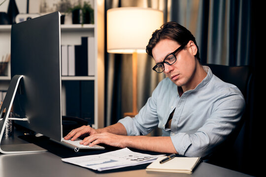 Smart businessman analyzing business paragraph dynamic database marketing analysis plan surrounded paper sheet and pc monitor report to compare with document data at home office at night. Pecuniary.