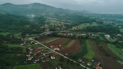 Wide aerial view of a Serbian valley with villages, plowed farmland, and mountain backdrop under...