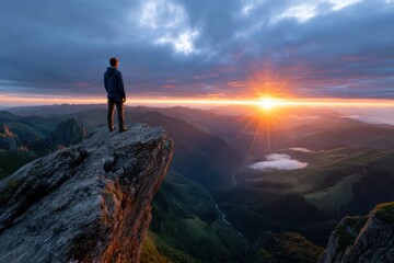 Man stands on rocky cliff overlooking valley during sunset in picturesque landscape