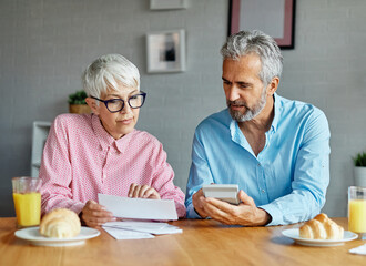 Senior couple checking bills and calculating expenses using a calculator at home, debt taxes and...