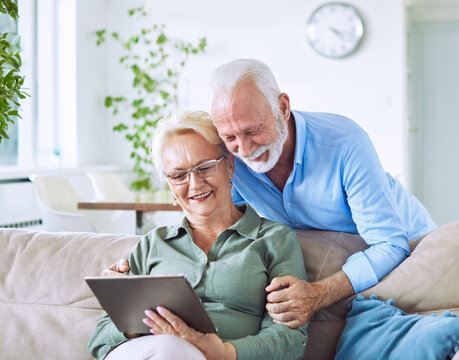 Portrait of a lovely senior mature couple together holding a tablet on sofa at home - Powered by Adobe