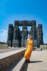A girl in a yellow dress stands at the monument of the chronicles of Georgia