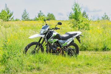 Off-road enduro motorcycle stands next to a country road in the middle of a field in tall grass